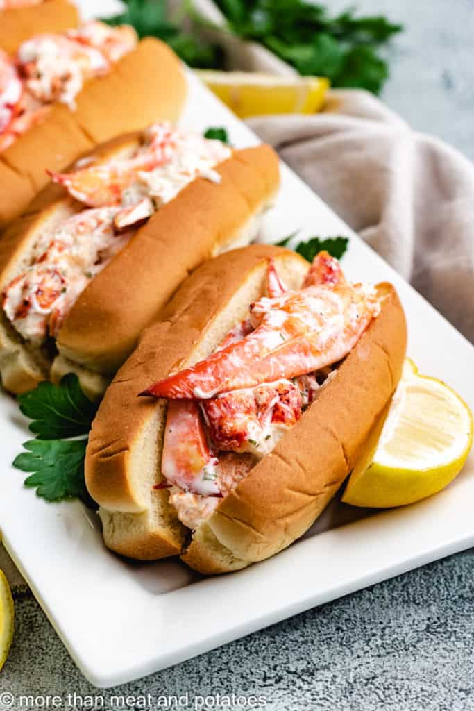 Lobster rolls on a platter with lemon wedges.