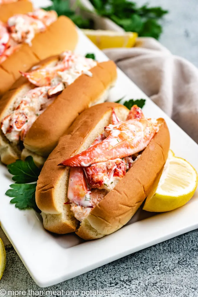 Lobster rolls on a platter with lemon wedges.