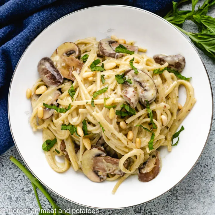 Top down view of pasta on a plate with mushrooms and pine nuts.