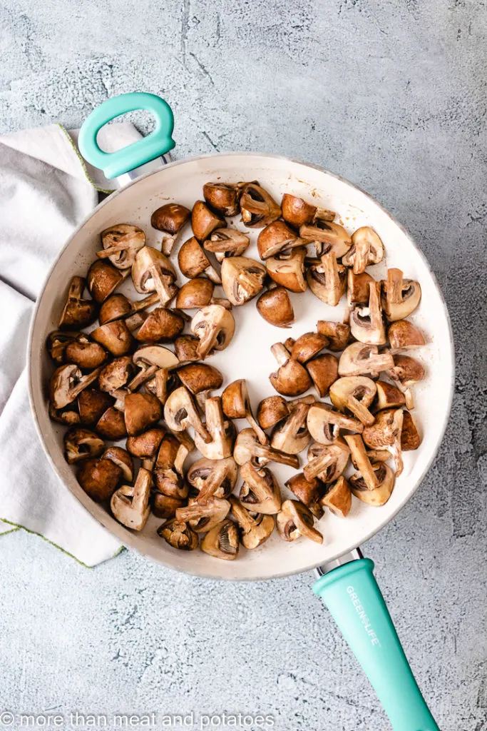 Top down view of mushrooms cooking in a skillet.