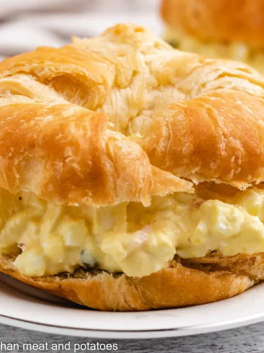 Egg salad on a croissant on a white plate.