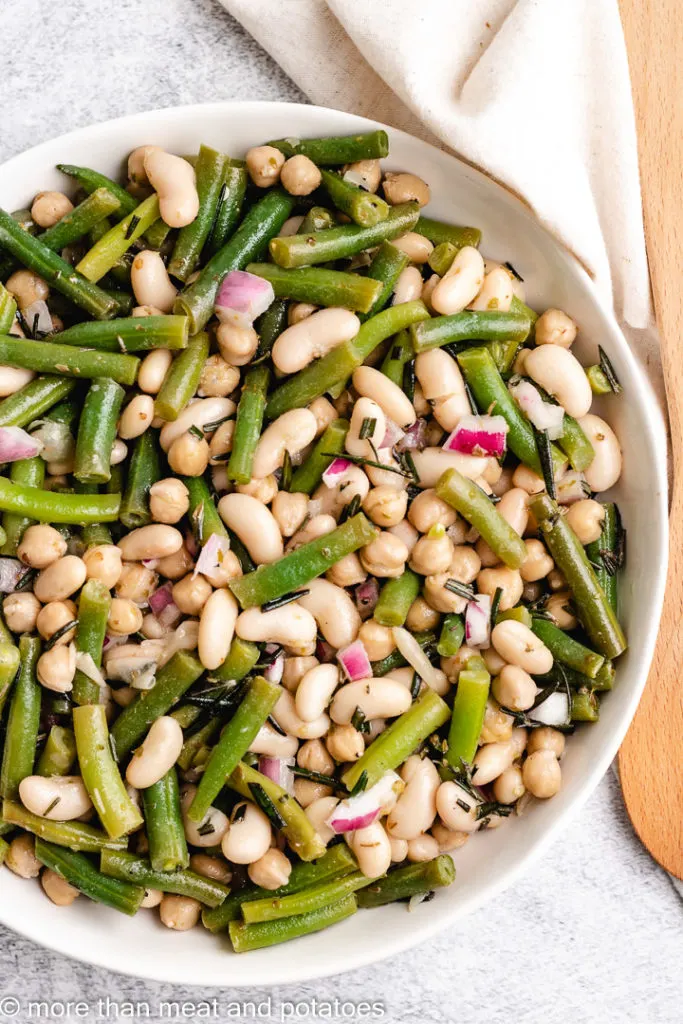 Top down view of bean salad next to a wooden spoon.