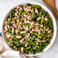 Three bean salad next to a large wooden spoon.