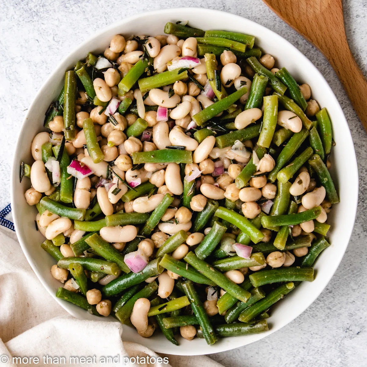 Three bean salad next to a large wooden spoon.