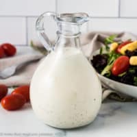 Close up of ranch dressing next to tomatoes and salad.