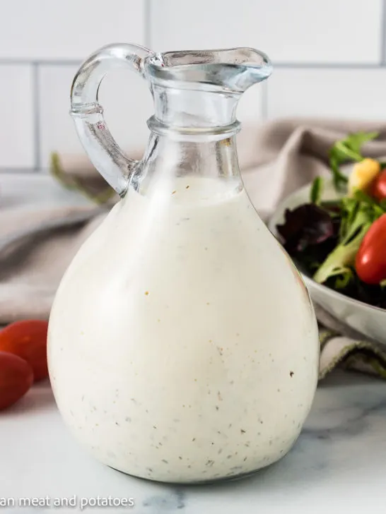 Close up of ranch dressing next to tomatoes and salad.