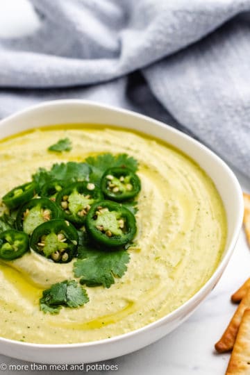 Close up view of hummus topped with jalapenos in a white bowl.