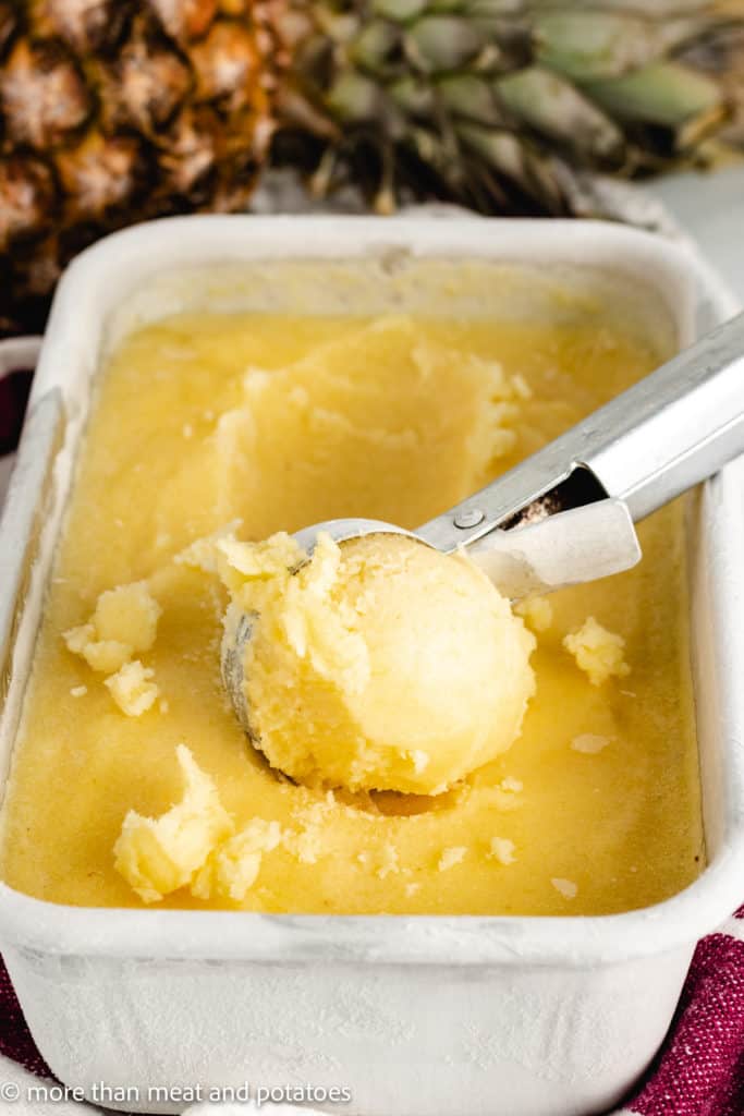 Pineapple sorbet being scooped from a pan.