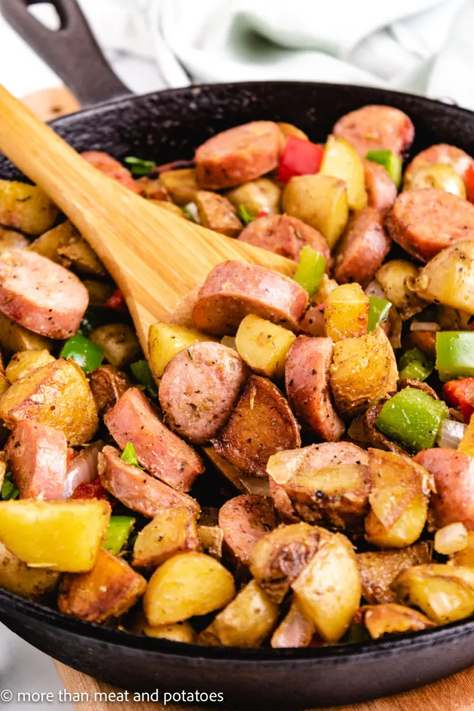 Close up view of sausage and potatoes on a wooden spoon.