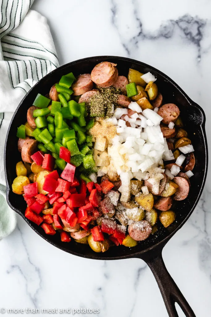 Top down view of peppers and onion being added to a skillet.