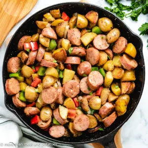 Top down view of sausage potatoes and peppers in cast iron.