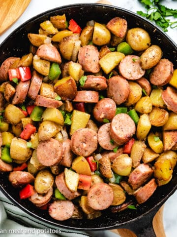Top down view of sausage potatoes and peppers in cast iron.