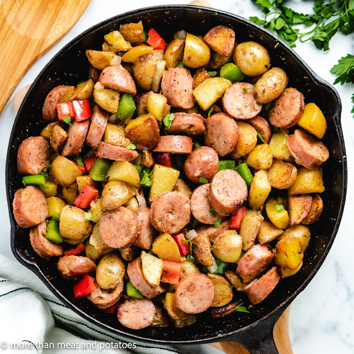 Top down view of sausage potatoes and peppers in cast iron.