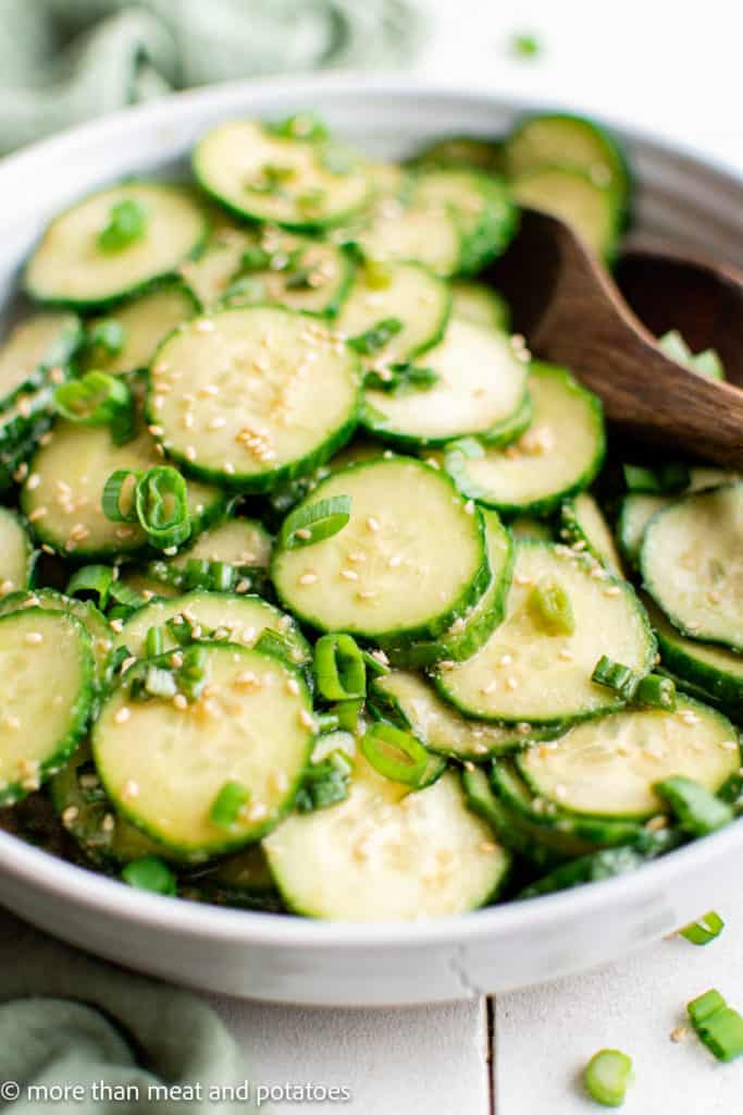 Large bowl of sliced cucumbers with asian dressing.