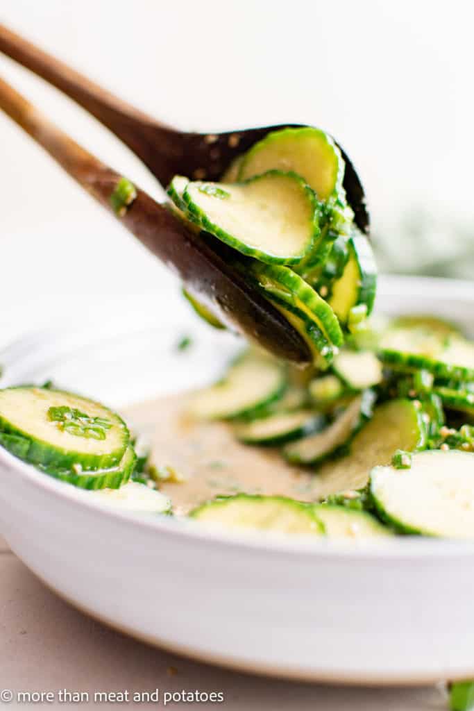 Cucumber salad being scooped with spoons.
