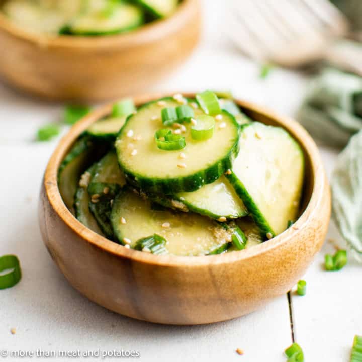 Bamboo bowl filled with sliced cucumbers and dressing.
