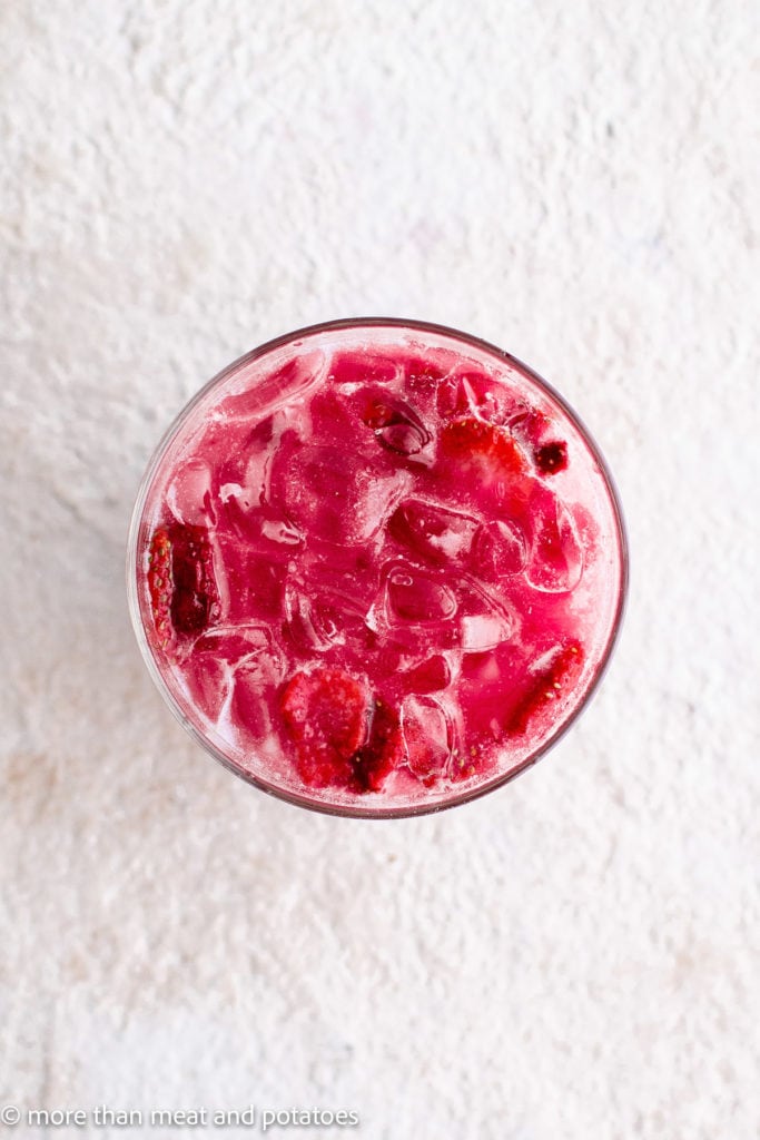 Top down view of pink drink mixed in a glass with ice.