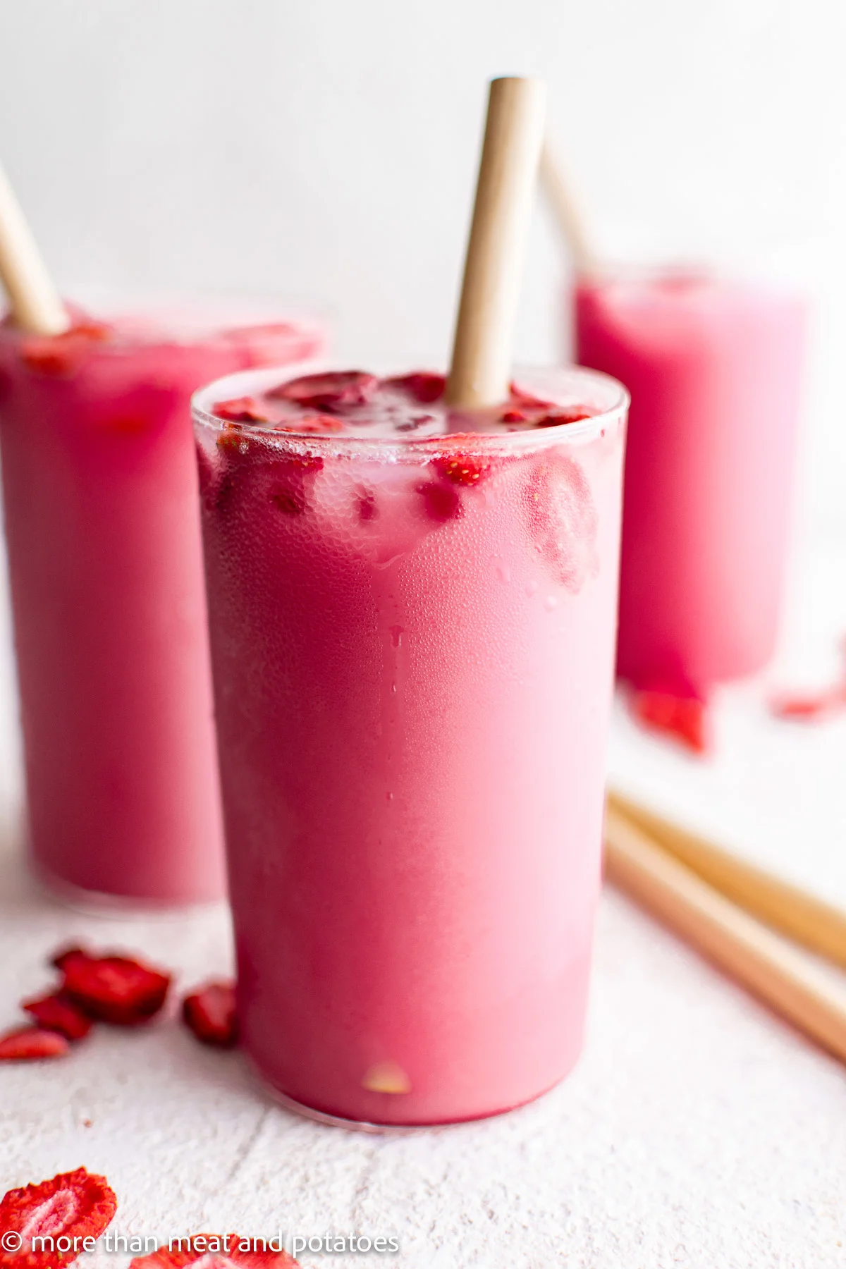 Three tall glasses with pink drink and straws.