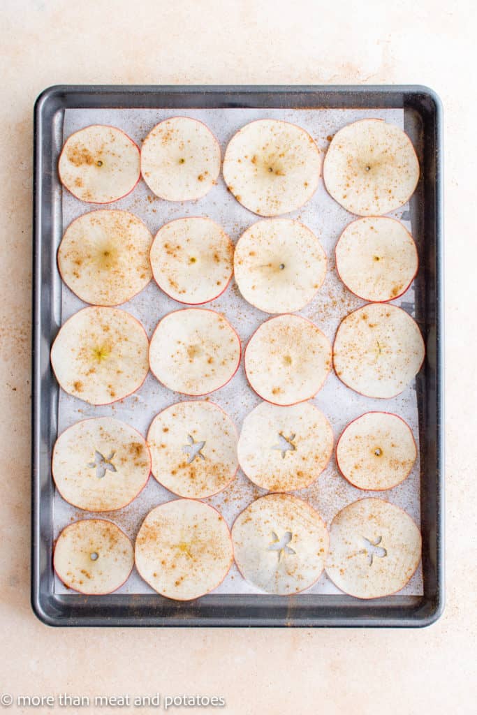 Top down view of raw apple slices sprinkled with cinnamon on a sheet pan.