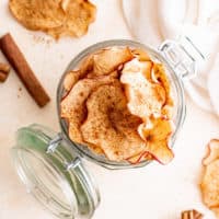 Top down view of a an open glass jar filled with dehydrated apple chips.