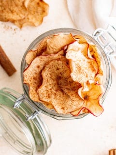 Top down view of a an open glass jar filled with dehydrated apple chips.