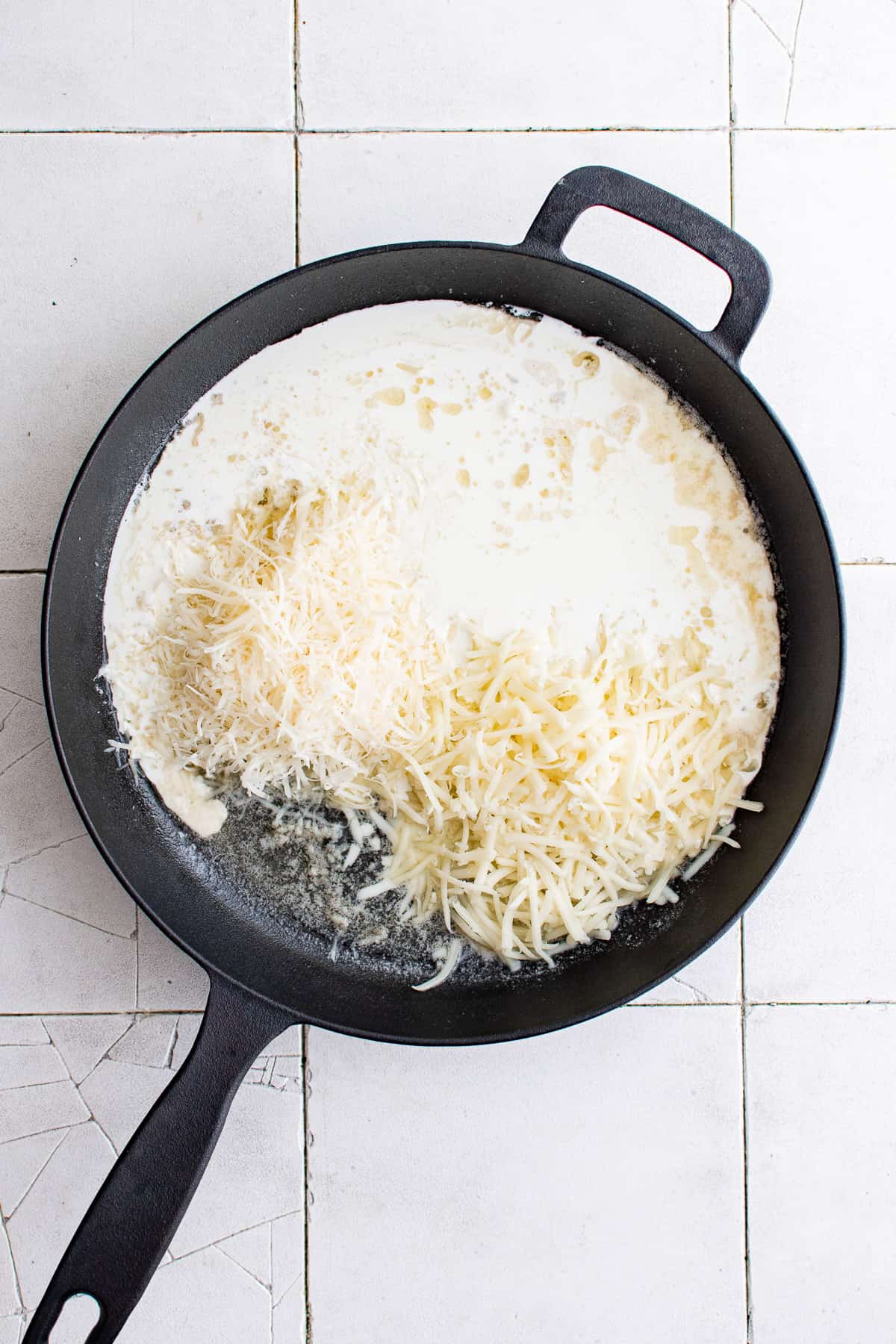Top down view cream sauce and shredded cheese in a pan.
