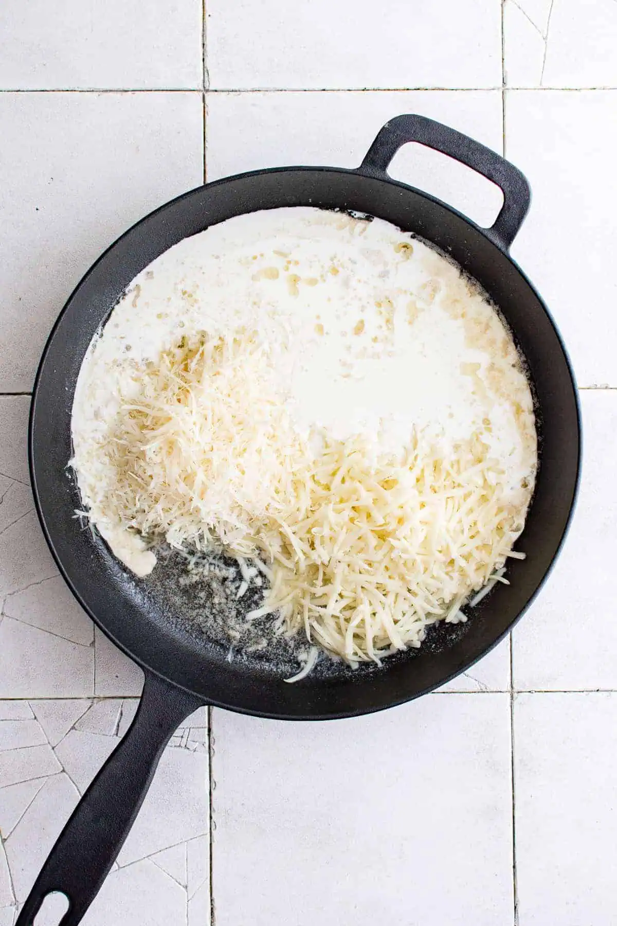 Top down view cream sauce and shredded cheese in a pan.