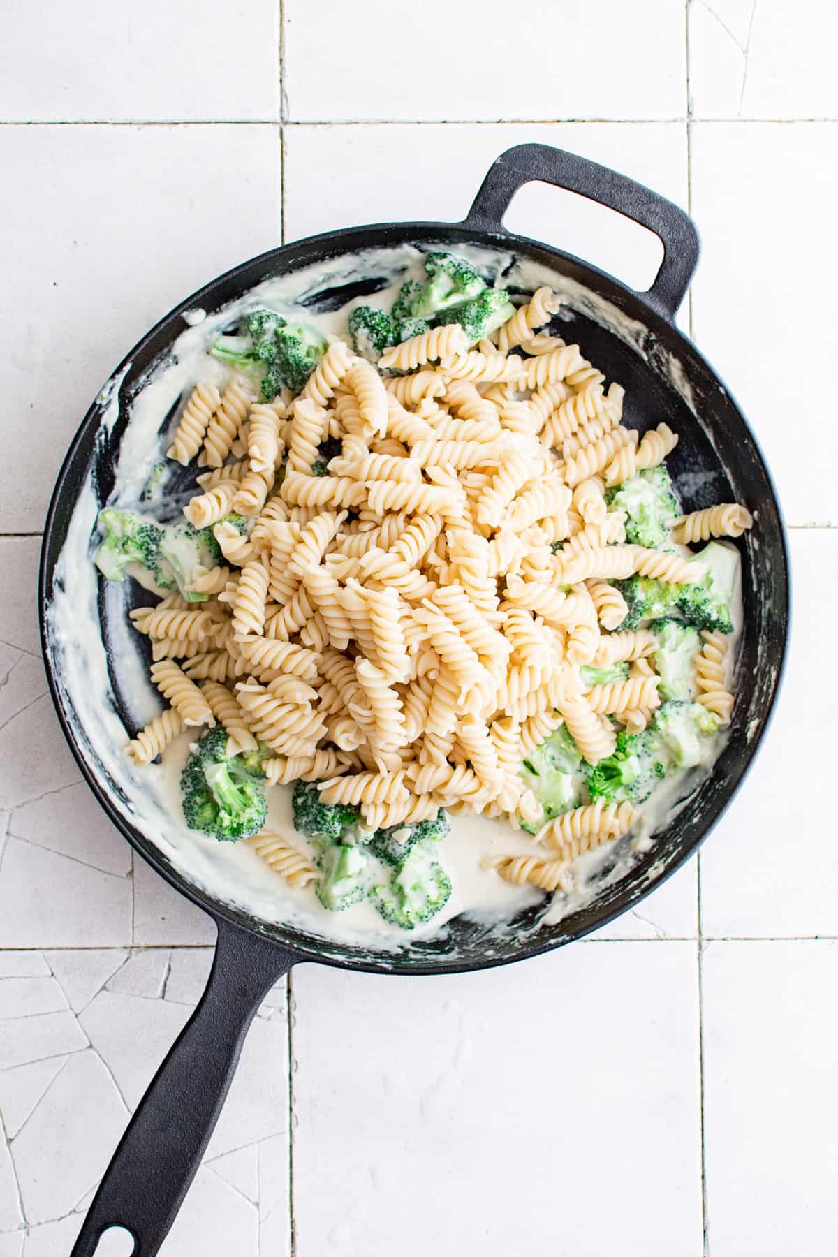 Top down view of pasta noodles on top of cream sauce with broccoli.