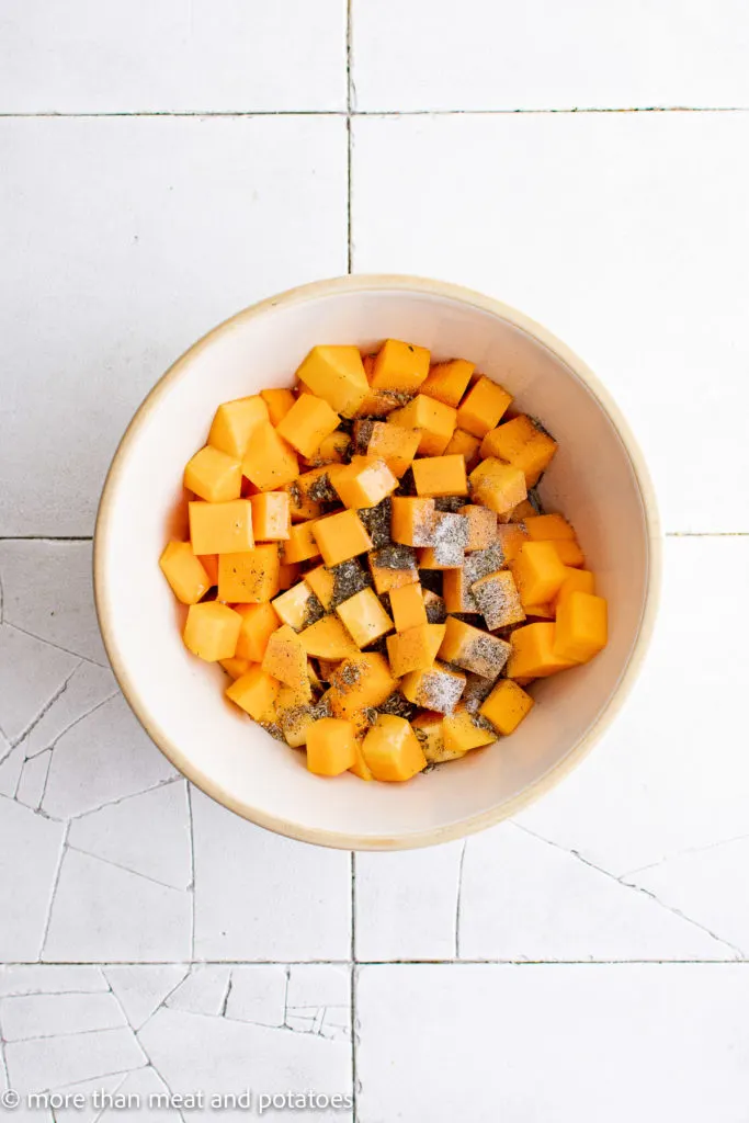 Top down view of butternut squash with seasonings in a bowl.