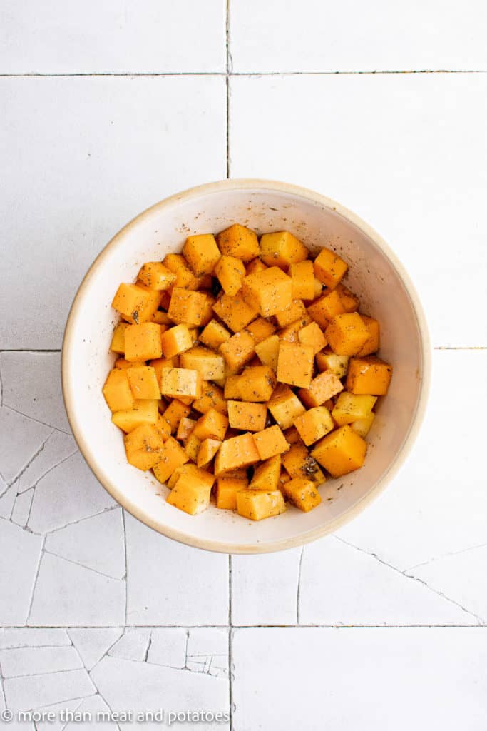 Top down view of butternut squash tossed with seasonings in a bowl.