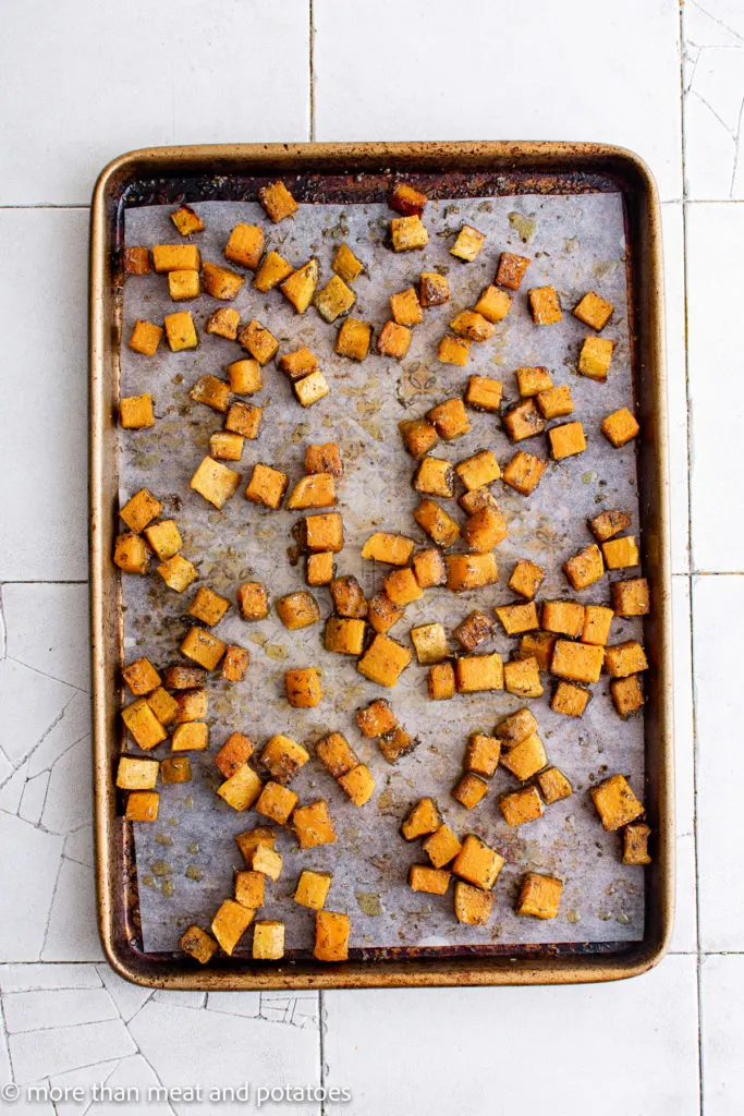 Top down view of seasoned butternut squash on a baking sheet.