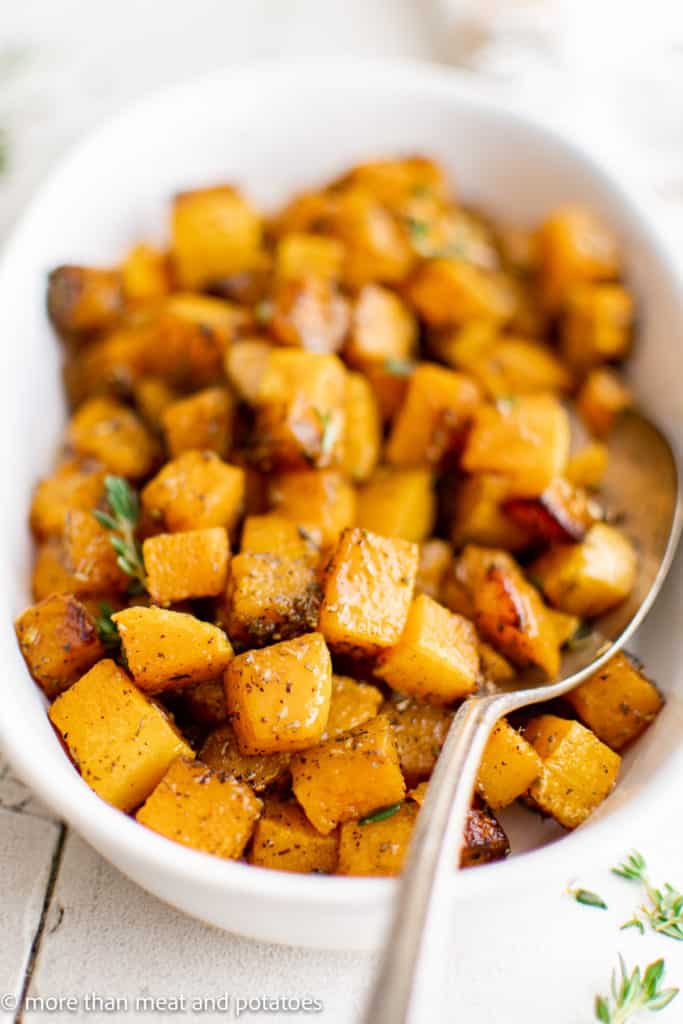 Close up of a platter of roasted butternut squash with a serving spoon.