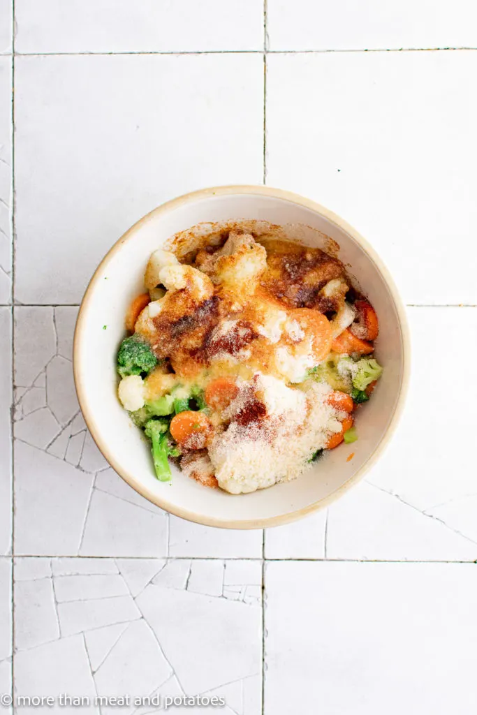 Top down view of mixed frozen vegetables in a bowl with seasonings.