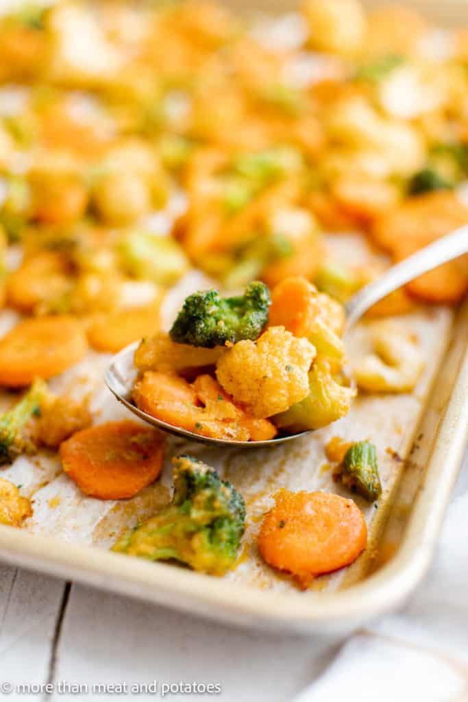 Roasted vegetables being scooped off of a sheet pan.