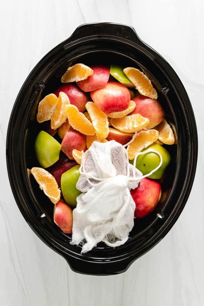 Top down view of apples, oranges, and spices in a slow cooker.