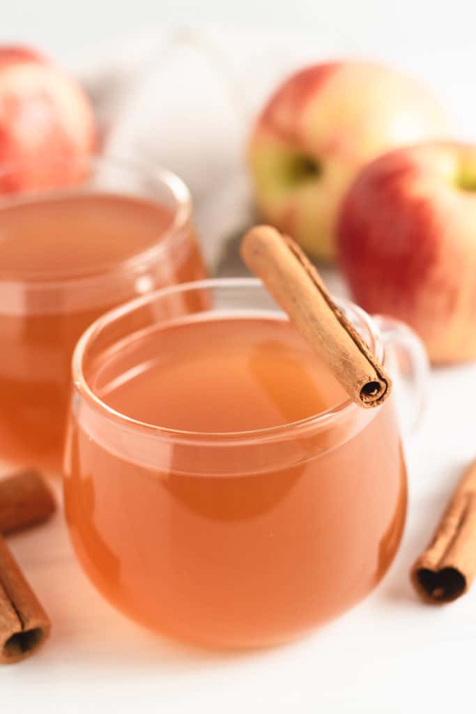 Glass mug filled with cider and a cinnamon stick.