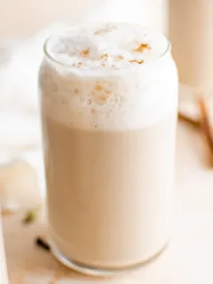 Glass of chai latte with frothed milk and cinnamon sticks.