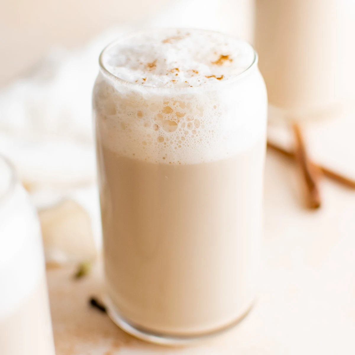 Glass of chai latte with frothed milk and cinnamon sticks.