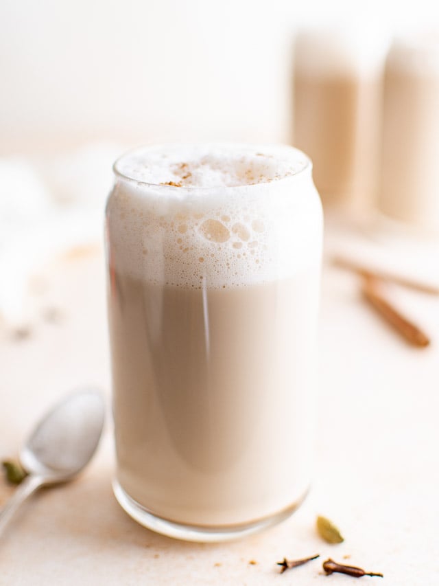 Tall glass of chai latte with cinnamon sticks.