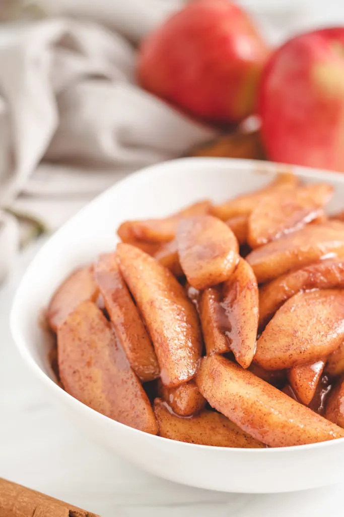 Cinnamon apples next to fresh apples in a bowl.