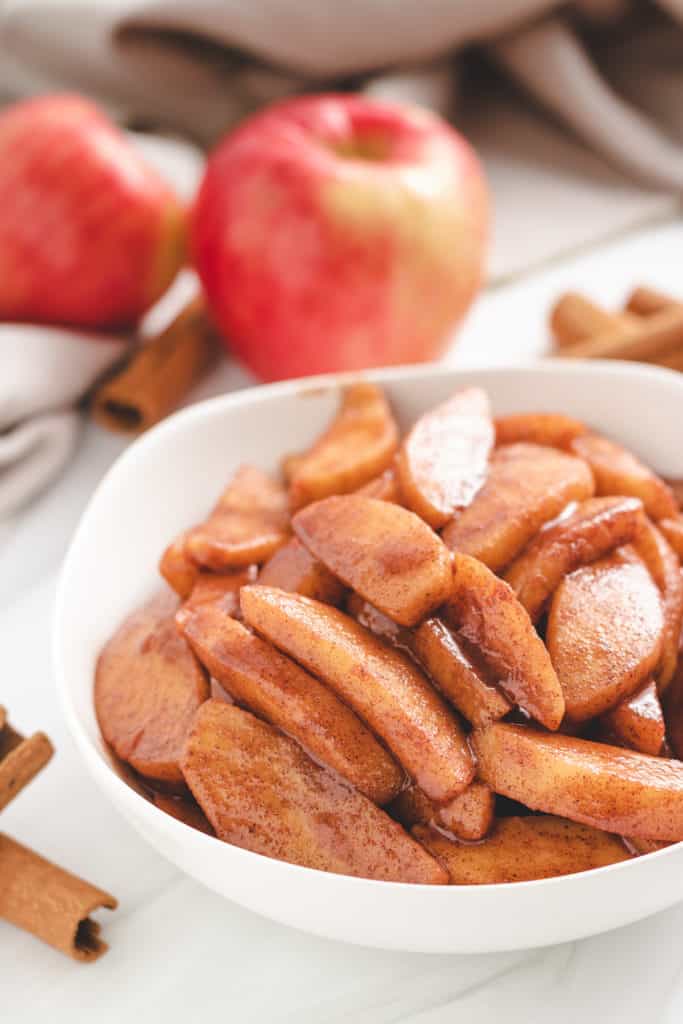 Sliced apples cooked in cinnamon in a white bowl.