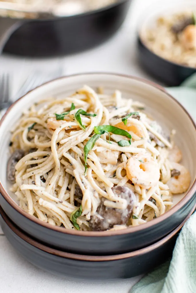 Black bowl filled with mushroom shrimp pasta.