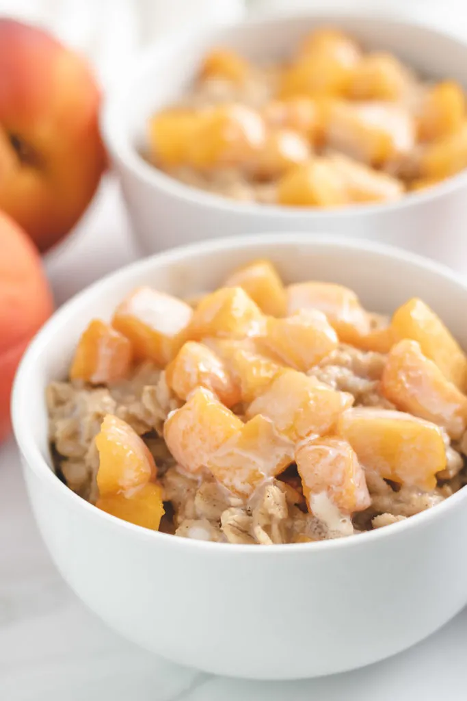 Close up view of oatmeal topped with peaches in a white bowl.