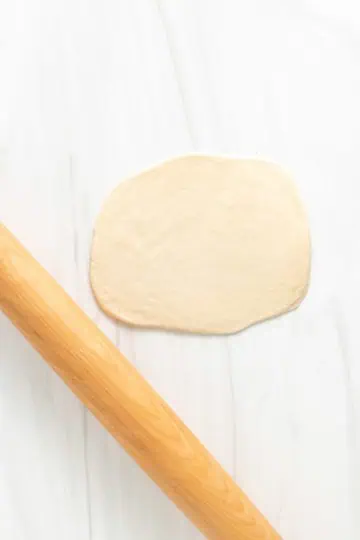 Top down view of naan dough rolled out with a rolling pin.