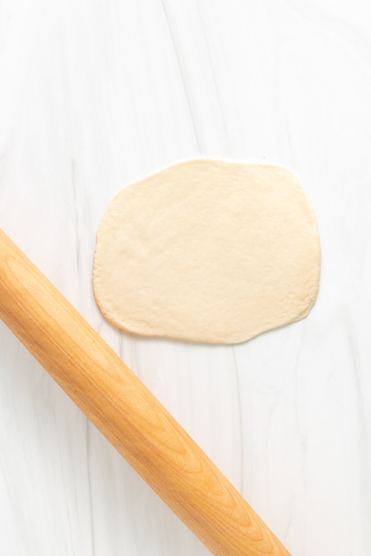 Top down view of naan dough rolled out with a rolling pin.