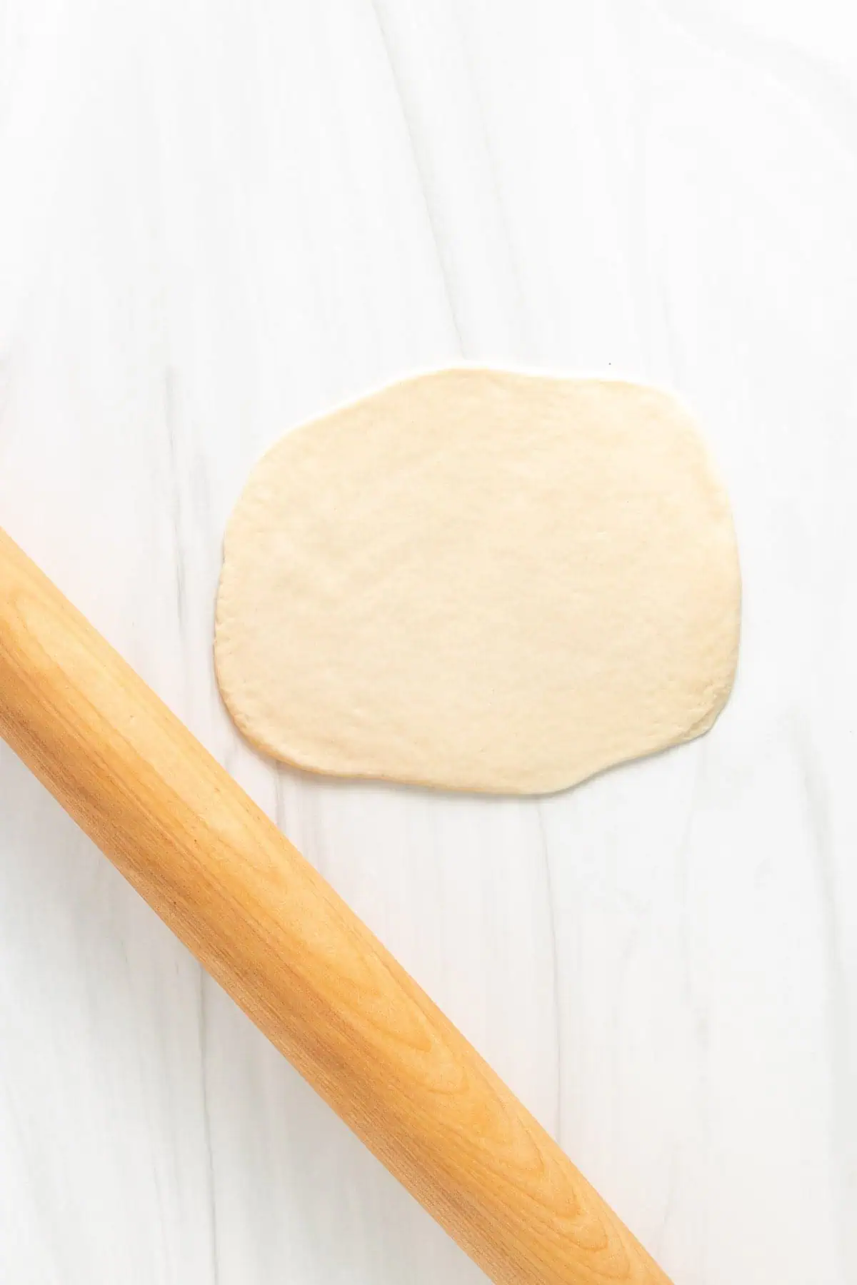 Top down view of naan dough rolled out with a rolling pin.