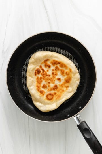 Top down view of sourdough naan bread in a pan.