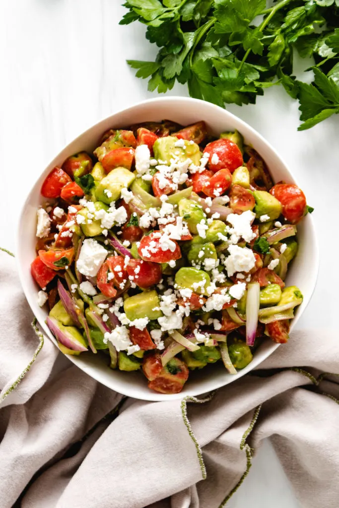 Top down view of tomato avocado salad with gray linens.