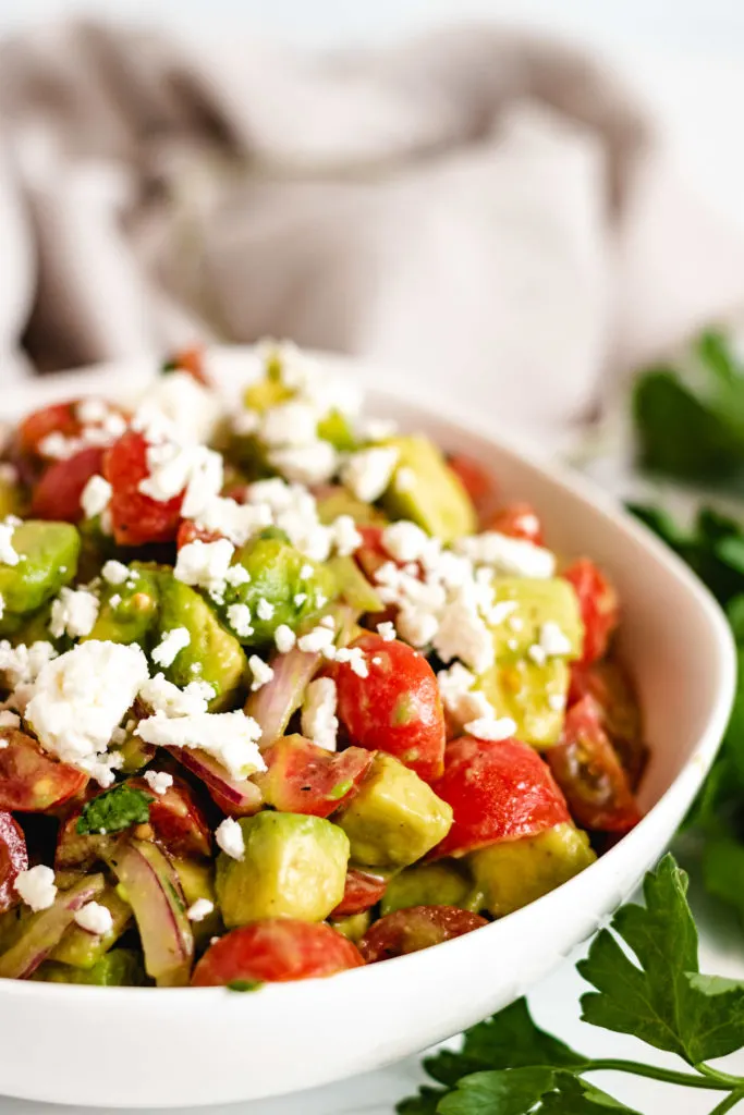 Close up of tomato avocado feta salad in a white bowl.