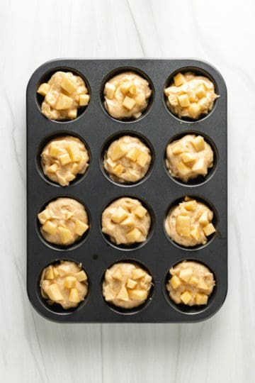 Top down view of muffin batter dotted with apples.